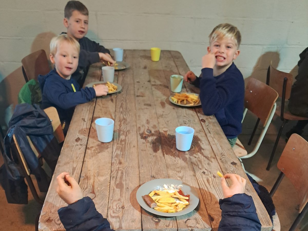 Kampkinderen aan de lange hoevebank met de warme lunch